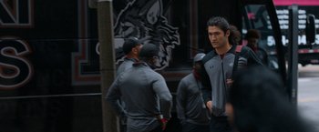 Movie still from “National Champions” (2021), directed by Ric Roman Waugh – A group of men standing next to each other on a street; Medium shot, Over the shoulder angle