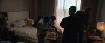 Movie still from “National Champions” (2021), directed by Ric Roman Waugh – A group of people sitting on a bed with a box of pizza; Medium shot, Over the shoulder angle