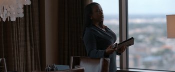 Movie still from “National Champions” (2021), directed by Ric Roman Waugh – A woman standing in front of a window holding a remote control; Medium shot, Low angle