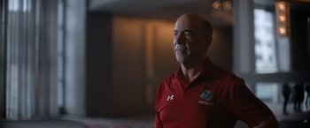 Movie still from “National Champions” (2021), directed by Ric Roman Waugh – An older man in a red shirt is looking off into the distance; Close Up shot, Low angle