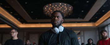 Movie still from “National Champions” (2021), directed by Ric Roman Waugh – A man with a beard wearing headphones looking up; Close Up shot, Low angle