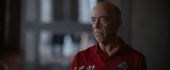 Movie still from “National Champions” (2021), directed by Ric Roman Waugh – A bald man in a red shirt is looking at the camera; Close Up shot, Over the shoulder angle