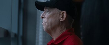 Movie still from “National Champions” (2021), directed by Ric Roman Waugh – An older man wearing a red shirt and a black hat; Close Up shot, Low angle