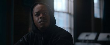 Movie still from “National Champions” (2021), directed by Ric Roman Waugh – A man wearing a black hooded jacket looking into the distance; Close Up shot, Low angle