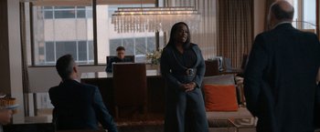 Movie still from “National Champions” (2021), directed by Ric Roman Waugh – A woman standing in front of a table in a living room; Medium shot, Over the shoulder angle