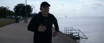 Movie still from “National Champions” (2021), directed by Ric Roman Waugh – A man running near the water on a cloudy day; Medium shot, Low angle