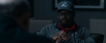 Movie still from “National Champions” (2021), directed by Ric Roman Waugh – A man with a beard wearing glasses and a hat; Close Up shot, Over the shoulder angle