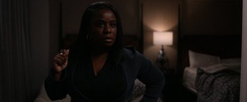 Movie still from “National Champions” (2021), directed by Ric Roman Waugh – A woman standing next to a lamp in a dark room; Medium shot, Over the shoulder angle
