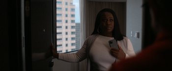 Movie still from “National Champions” (2021), directed by Ric Roman Waugh – A woman standing in front of a window holding a cell phone; Medium shot, Over the shoulder angle