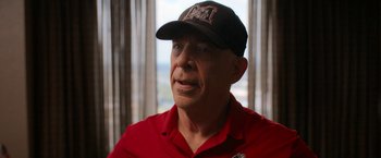 Movie still from “National Champions” (2021), directed by Ric Roman Waugh – An older man wearing a baseball cap and a red shirt; Close Up shot, Over the shoulder angle