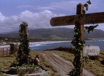 Movie still from “National Velvet” (1944), directed by Clarence Brown – A person sitting on the side of a road next to a sign post; Extreme Wide shot, High angle