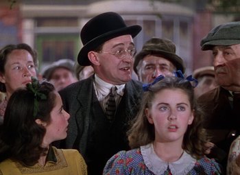 Movie still from “National Velvet” (1944), directed by Clarence Brown – An older man in a suit and hat surrounded by young people; Medium shot, Over the shoulder angle