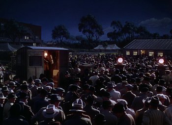 Movie still from “National Velvet” (1944), directed by Clarence Brown – A crowd of people standing in front of a building at night; Extreme Wide shot, High angle
