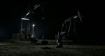 Movie still from “Near Dark” (1987), directed by Kathryn Bigelow – A man kneeling down in front of an oil well; Extreme Wide shot, Low angle