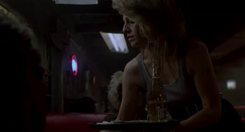 Movie still from “Near Dark” (1987), directed by Kathryn Bigelow – A woman sitting at a table with a tray of food and a bottle; Medium shot, Low angle