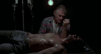 Movie still from “Near Dark” (1987), directed by Kathryn Bigelow – A man sitting in front of a shirtless man in a dark room; Medium shot, High angle