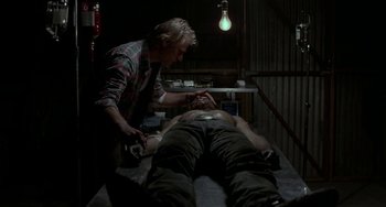 Movie still from “Near Dark” (1987), directed by Kathryn Bigelow – A man is getting a tattoo on a man's chest; Medium shot, Over the shoulder angle