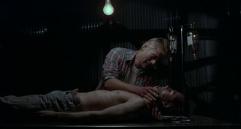 Movie still from “Near Dark” (1987), directed by Kathryn Bigelow – A man is laying on a table with a knife in his hand; Medium shot, Low angle