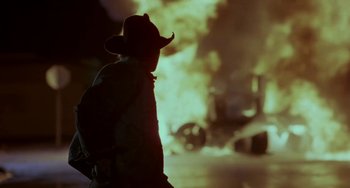 Movie still from “Near Dark” (1987), directed by Kathryn Bigelow – A man in a cowboy hat standing in front of a burning car; Medium shot, Low angle