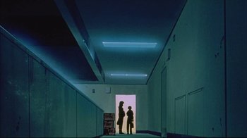 Movie still from “Neon Genesis Evangelion: Death & Rebirth” (1997), directed by Tensai Okamura – Two people are standing in a hallway with a neon light; Wide shot, Low angle