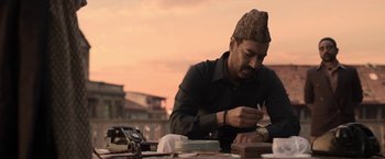 Movie still from “Gangubai Kathiawadi” (2022), directed by Sanjay Leela Bhansali – A man sitting at an outdoor table with papers and a phone; Medium shot, Low angle