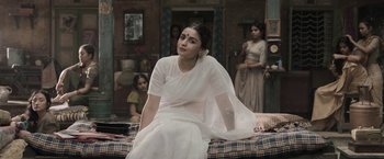 Movie still from “Gangubai Kathiawadi” (2022), directed by Sanjay Leela Bhansali – A woman sitting on top of a bed wearing a white dress; Medium shot, Low angle