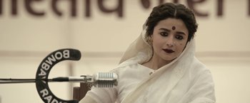 Movie still from “Gangubai Kathiawadi” (2022), directed by Sanjay Leela Bhansali – A woman in a white sari is holding a microphone; Close Up shot, High angle