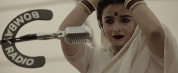 Movie still from “Gangubai Kathiawadi” (2022), directed by Sanjay Leela Bhansali – A woman in a white sari holding a microphone; Close Up shot, Low angle