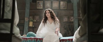 Movie still from “Gangubai Kathiawadi” (2022), directed by Sanjay Leela Bhansali – A woman sitting on top of a couch wearing a white dress; Medium shot, Low angle
