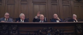 Movie still from “Neruda” (2016), directed by Pablo Larraín – Three men are sitting at a table in front of a wooden wall; Medium shot, Low angle