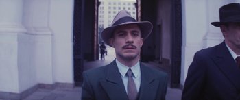 Movie still from “Neruda” (2016), directed by Pablo Larraín – A man wearing a suit and hat standing in front of a building; Close Up shot, Low angle