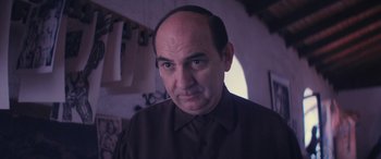 Movie still from “Neruda” (2016), directed by Pablo Larraín – A man with a bald head is looking at the camera; Close Up shot, Over the shoulder angle