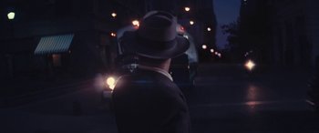 Movie still from “Neruda” (2016), directed by Pablo Larraín – A man wearing a hat walking down a street; Medium shot, Over the shoulder angle