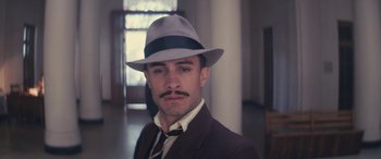 Movie still from “Neruda” (2016), directed by Pablo Larraín – A man in a suit and a hat is posing for a picture; Close Up shot, Low angle