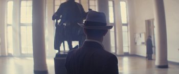 Movie still from “Neruda” (2016), directed by Pablo Larraín – A man wearing a hat looking at a statue; Medium shot, Over the shoulder angle