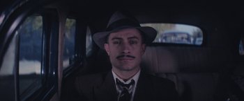 Movie still from “Neruda” (2016), directed by Pablo Larraín – A man in a suit and hat in the back of a car; Close Up shot, High angle