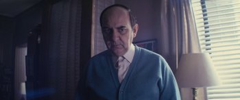 Movie still from “Neruda” (2016), directed by Pablo Larraín – An older man wearing a blue sweater and a white tie; Close Up shot, Low angle