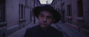 Movie still from “Neruda” (2016), directed by Pablo Larraín – A man wearing a hat standing on a street; Close Up shot, Low angle