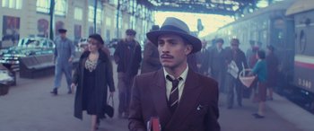 Movie still from “Neruda” (2016), directed by Pablo Larraín – A man in a suit and a hat is standing in front of a group of people; Medium shot, Low angle
