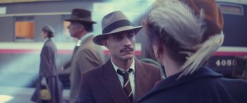 Movie still from “Neruda” (2016), directed by Pablo Larraín – A man wearing a suit and a hat talking to a woman; Close Up shot, Over the shoulder angle