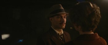 Movie still from “Neruda” (2016), directed by Pablo Larraín – A man in a suit and a hat is standing in the dark; Close Up shot, Over the shoulder angle