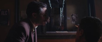 Movie still from “Neruda” (2016), directed by Pablo Larraín – A man in a suit and tie is looking at a microphone; Close Up shot, Over the shoulder angle