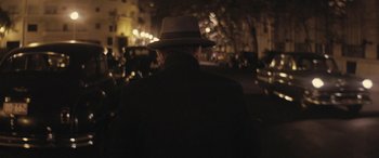 Movie still from “Neruda” (2016), directed by Pablo Larraín – A man wearing a hat standing in the dark; Close Up shot, Over the shoulder angle