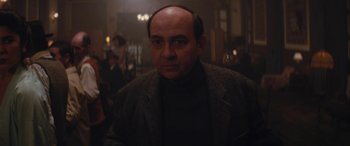 Movie still from “Neruda” (2016), directed by Pablo Larraín – A man with a bald head is standing in a room; Medium shot, Low angle