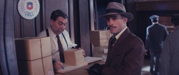 Movie still from “Neruda” (2016), directed by Pablo Larraín – A man sitting at a table in a suit and tie; Medium shot, Low angle