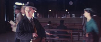 Movie still from “Neruda” (2016), directed by Pablo Larraín – A man in a hat and a tie holding a briefcase in front of people; Medium shot, Low angle