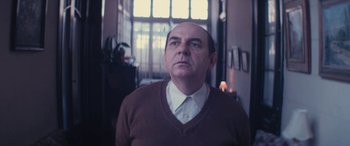 Movie still from “Neruda” (2016), directed by Pablo Larraín – A man in a brown sweater and a white shirt; Medium shot, Low angle