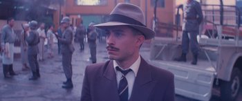 Movie still from “Neruda” (2016), directed by Pablo Larraín – A man in a suit and a hat is standing in the street; Close Up shot, Low angle