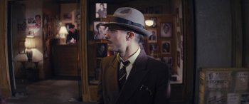 Movie still from “Neruda” (2016), directed by Pablo Larraín – A man wearing a suit and a hat in front of a wall; Close Up shot, Over the shoulder angle