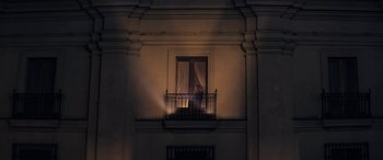 Movie still from “Neruda” (2016), directed by Pablo Larraín – A person standing on a balcony looking out a window at night; Extreme Wide shot, Low angle